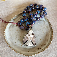 Symbolic talisman necklace with blue ceramic beads and a carved Thunderbird pendant on a ceramic dish.