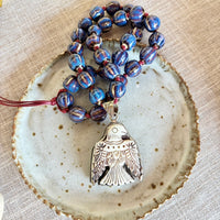 Symbolic beaded talisman necklace with a thunderbird pendant on a textured ceramic plate